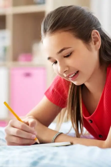 Homeschool girl writing in her journal laying on a bed