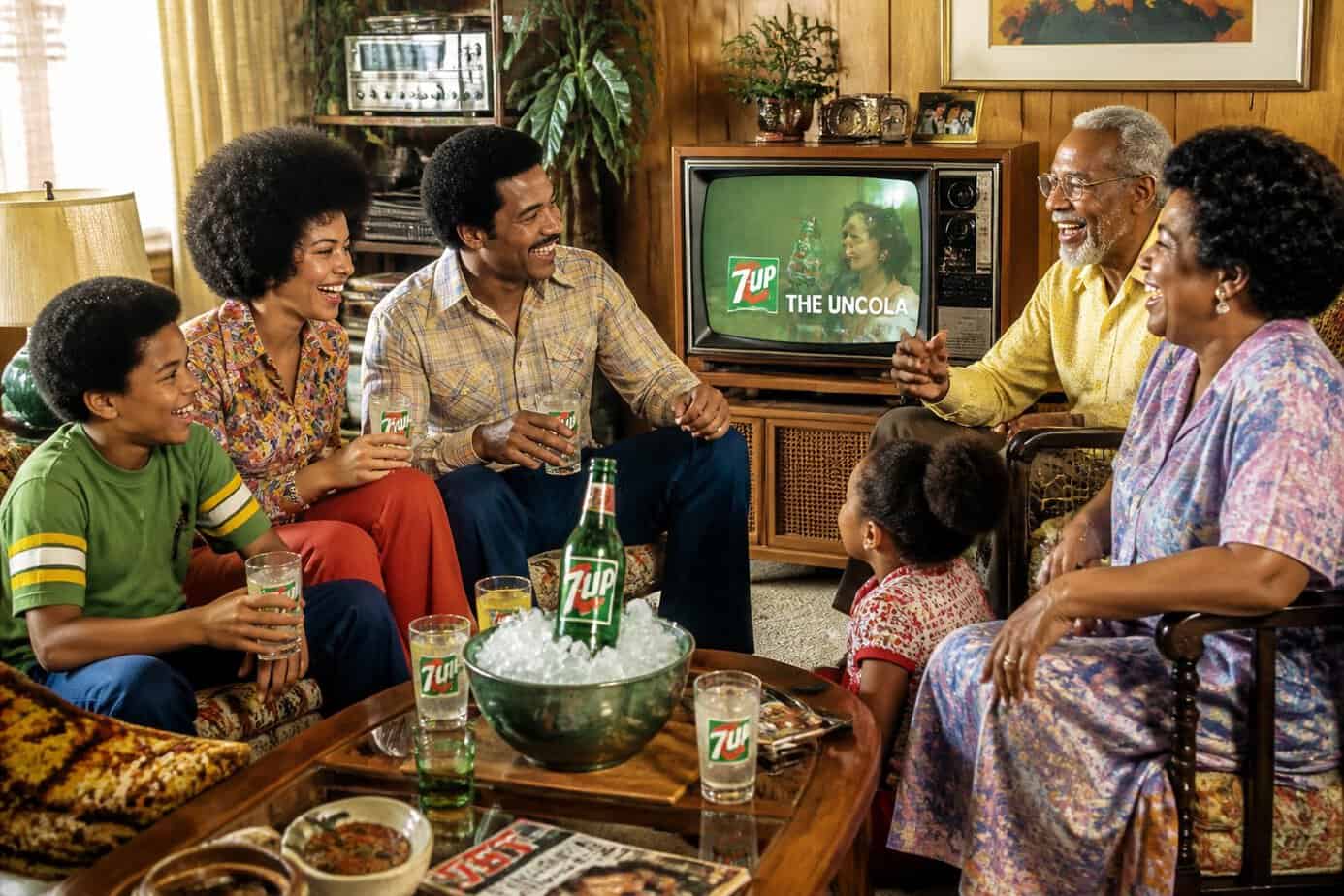 A multi-generational family smiling and enjoying 7UP in a retro living room with a vintage TV in the background.