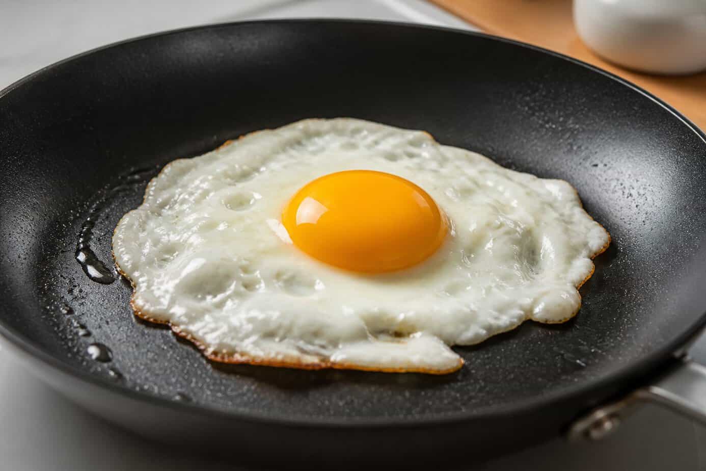 Close-up of a fried egg cooking in a pan with a bright yellow yolk and irregular white.