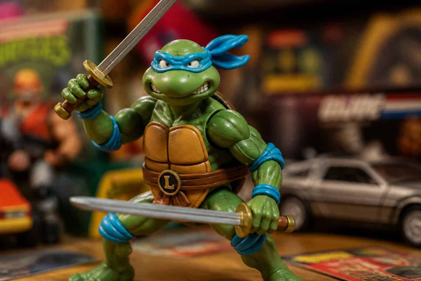 Close-up of a Leonardo Teenage Mutant Ninja Turtles action figure holding katanas with a blurred background of vintage toys.