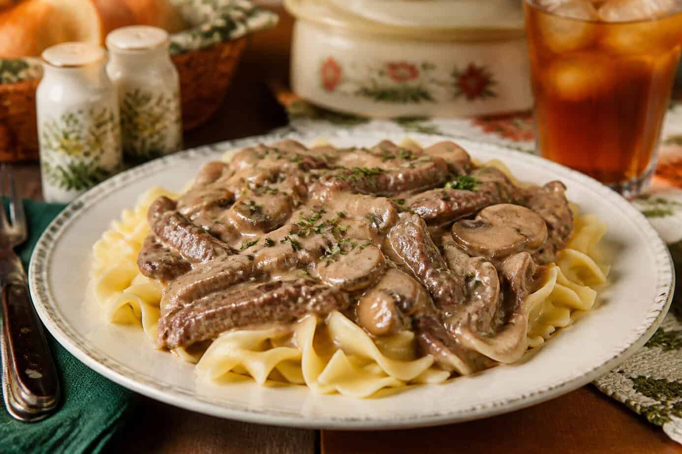 A plate of beef stroganoff with egg noodles on a wooden table set for a family meal.