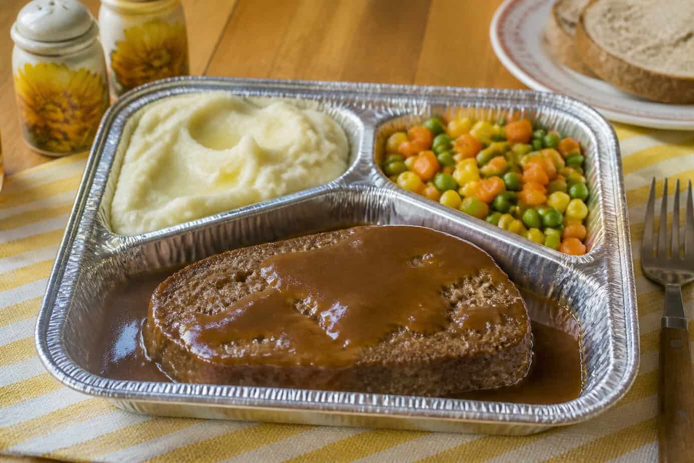 A TV dinner tray with meatloaf, mashed potatoes, and mixed vegetables on a kitchen table.
