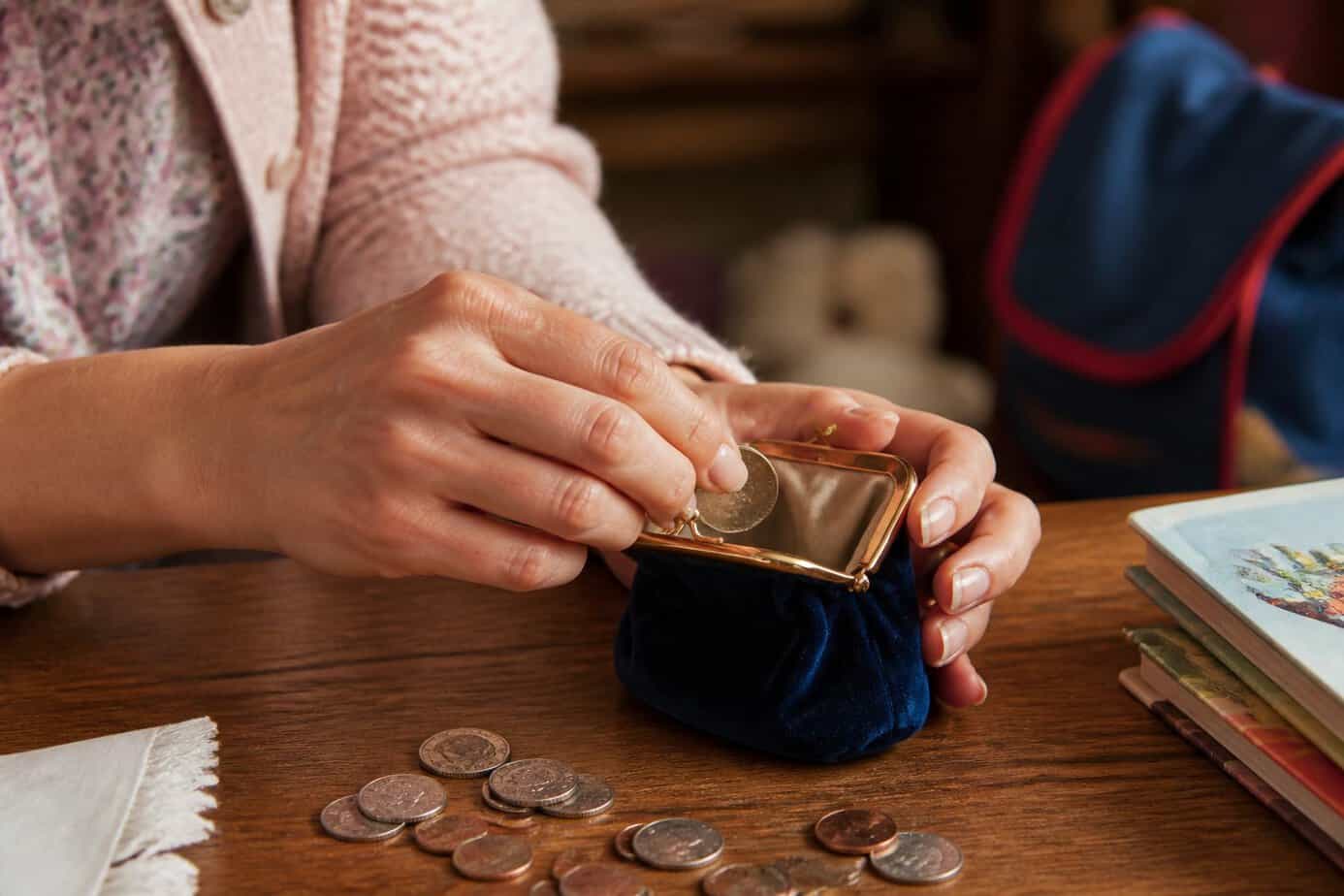 Hands filling a small coin purse with spare change on a wooden table.