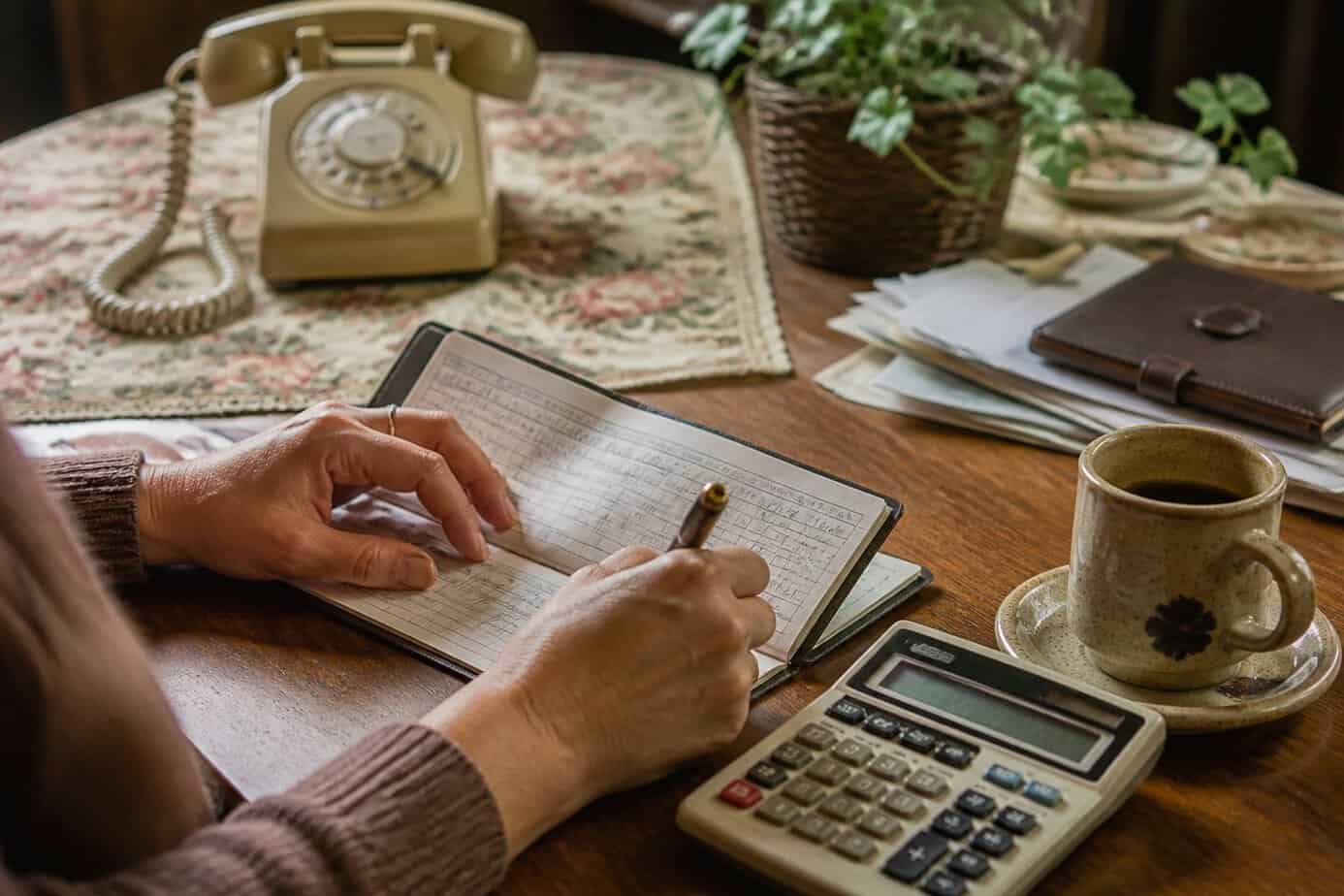 Hands balancing a checkbook by hand on a wooden table with a calculator nearby in a cozy home setting.