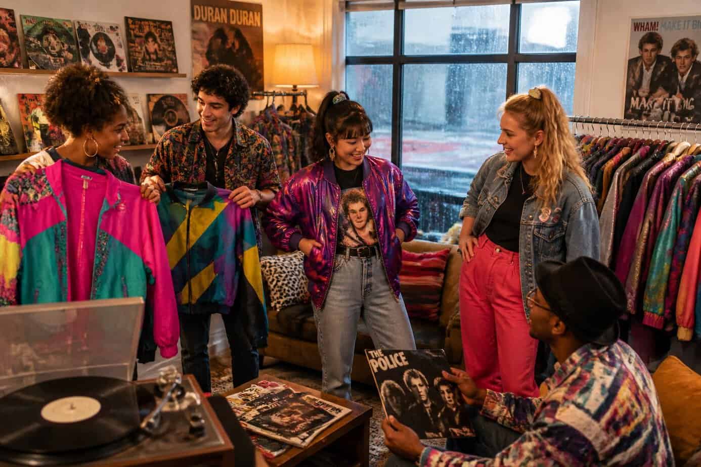 A group of young adults trying on vintage 1980s vinyl jackets indoors on a rainy day.