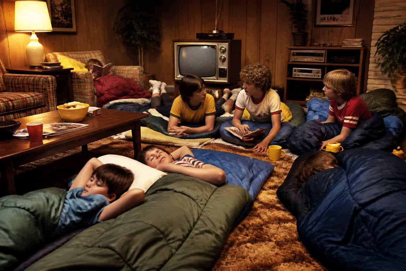 Children sleeping in sleeping bags on the living room floor surrounded by vintage 1970s decor.
