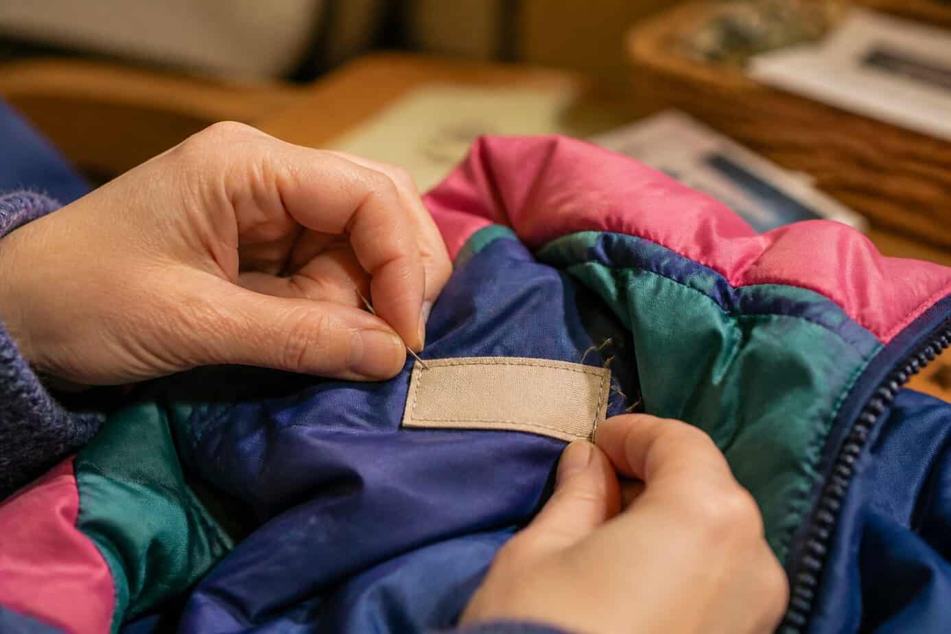Close-up of hands sewing a name tag into the inside of a child's jacket.