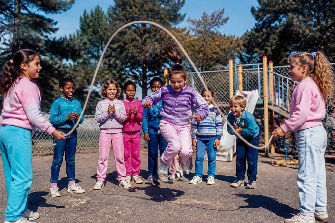 Children playing jump rope together in a school playground on a sunny day.