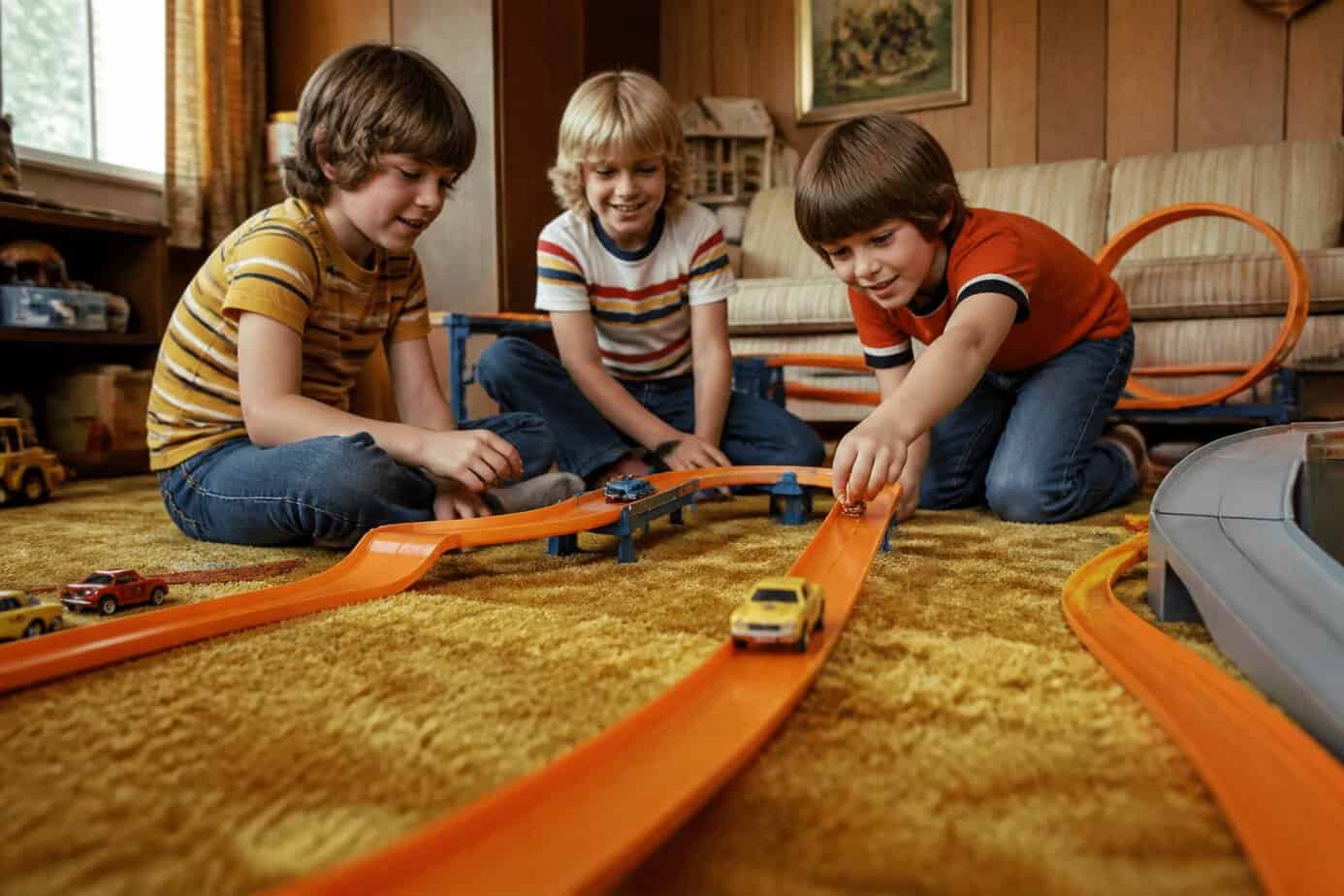 Children race miniature cars along colorful tracks on a living-room floor.