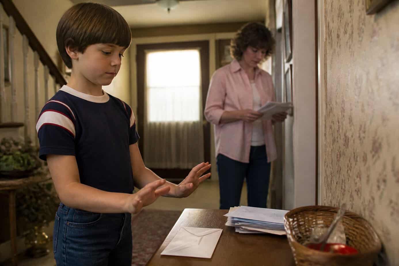 A child pauses beside a sealed envelope while an adult sorts mail in a home entryway.