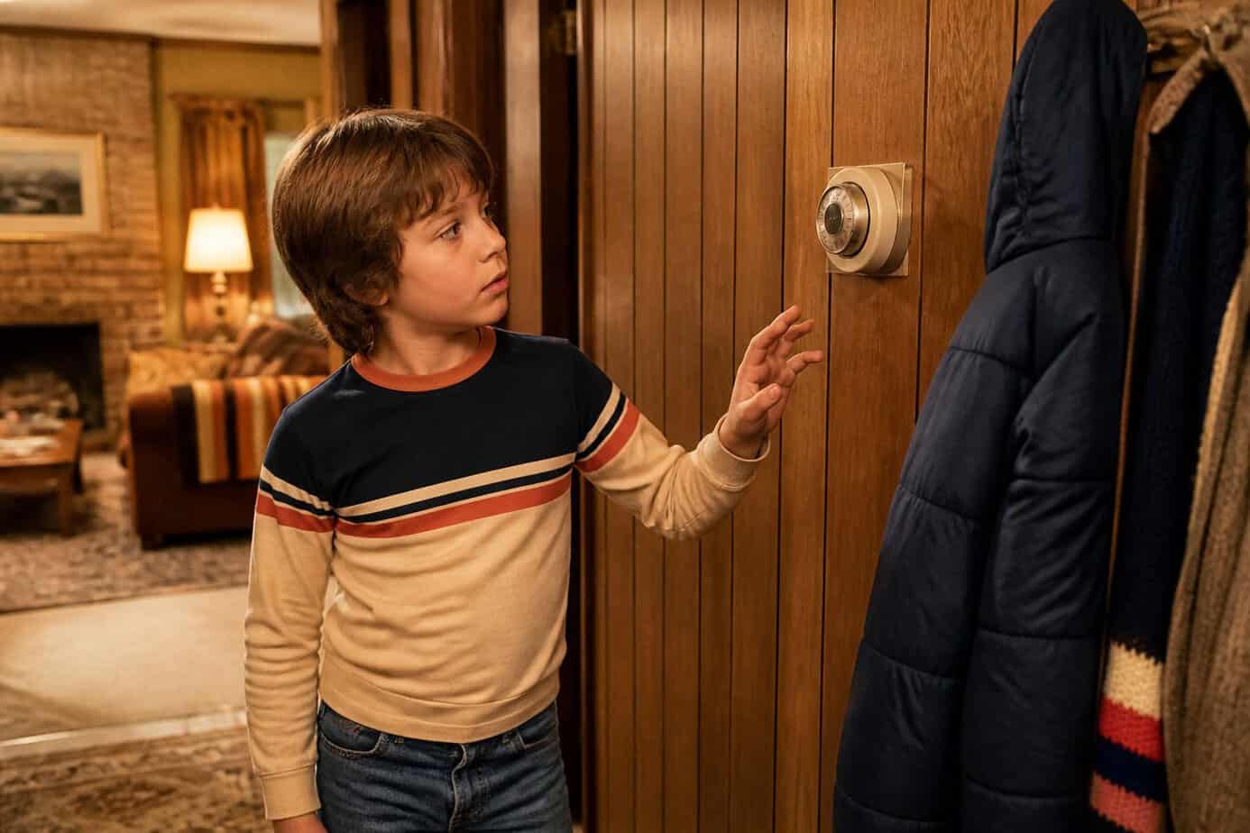 A child pauses beside a wall-mounted thermostat without touching it in a cozy retro hallway.