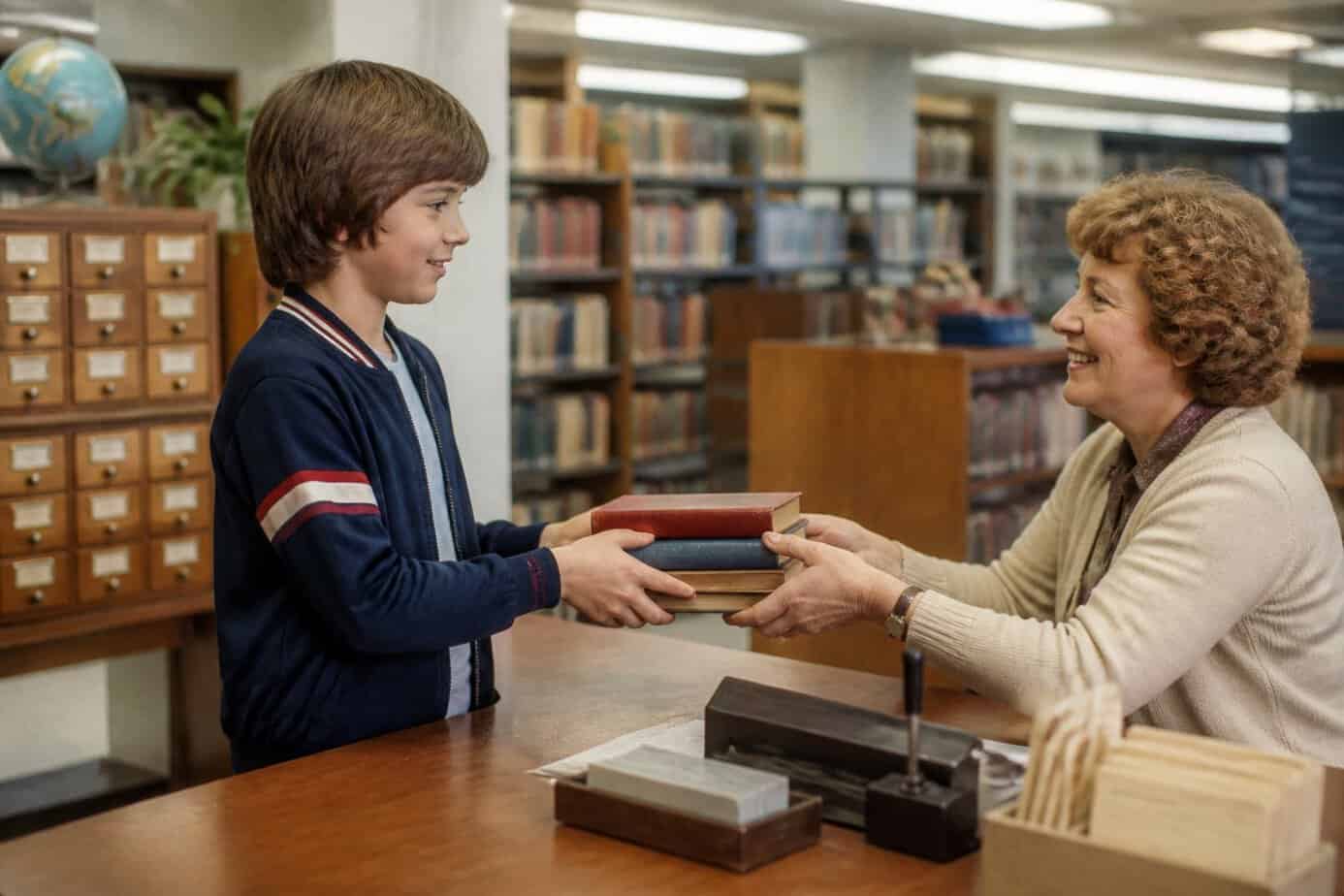 A child returns a stack of books to a librarian at a public library desk.