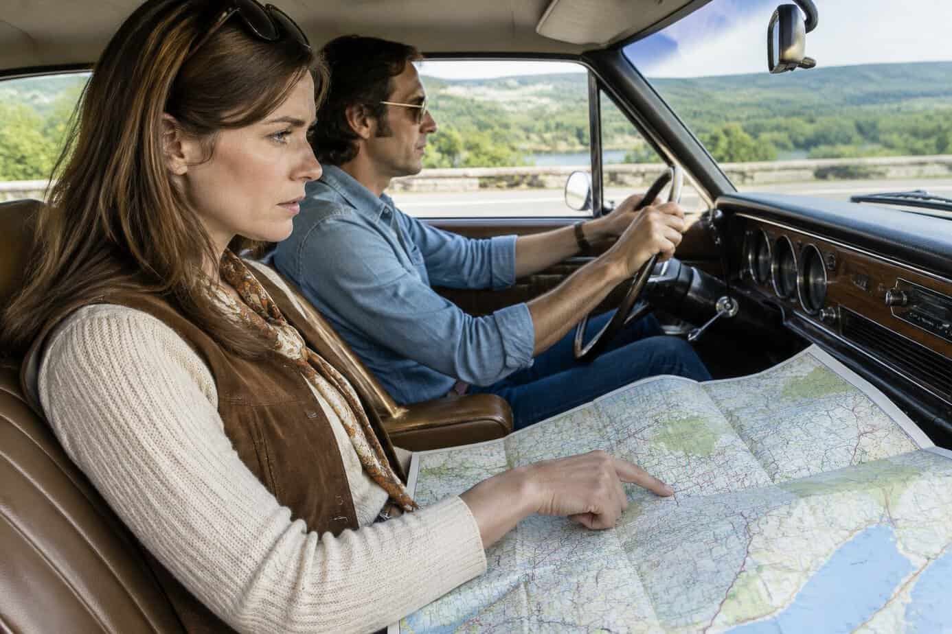 A woman follows a route on a paper map in the passenger seat of a car.