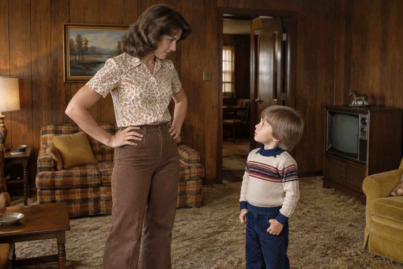 A young 1970s mother with her hands on her hips gives her little boy a firm look in a wood-paneled living room.