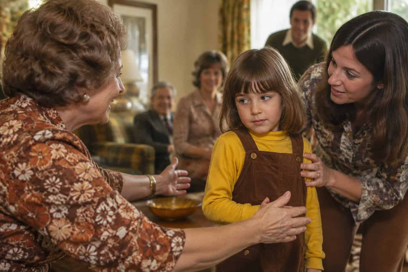 A hesitant child leans away as a relative offers a hug at a family gathering.