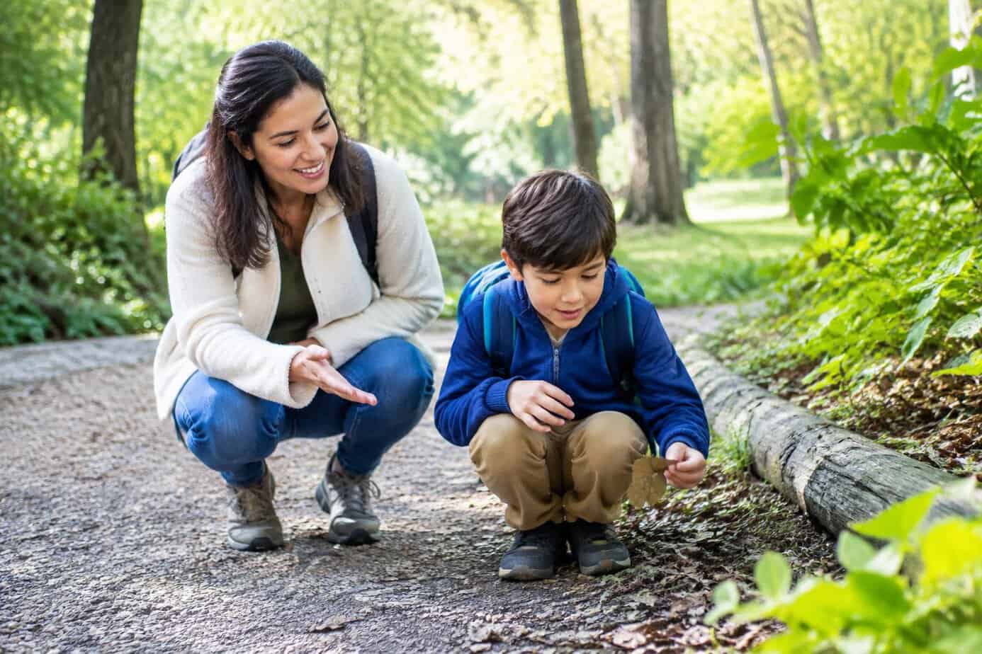 A parent watches as a child explores a leafy park trail.