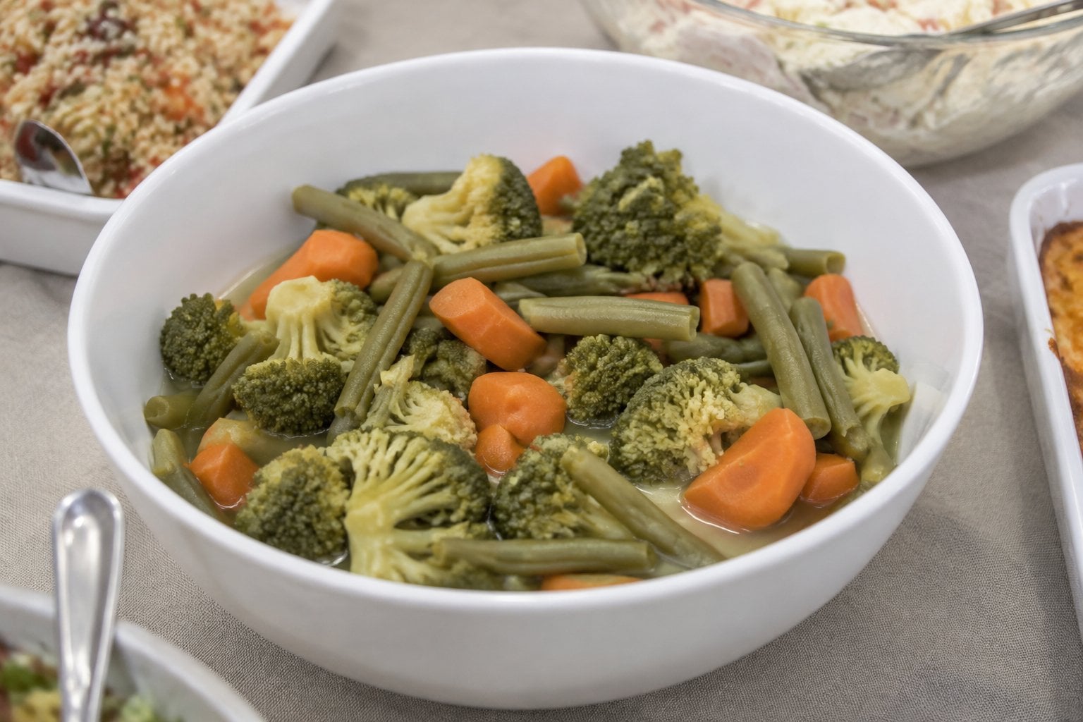 A bowl of pale boiled vegetables on a potluck buffet table.