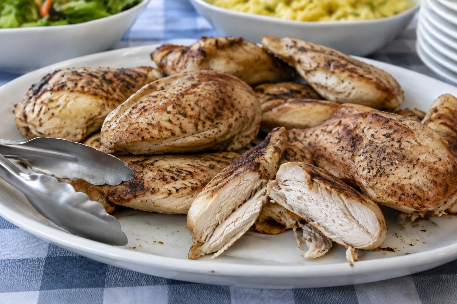 Dry baked chicken breasts sit on a serving platter at a buffet.