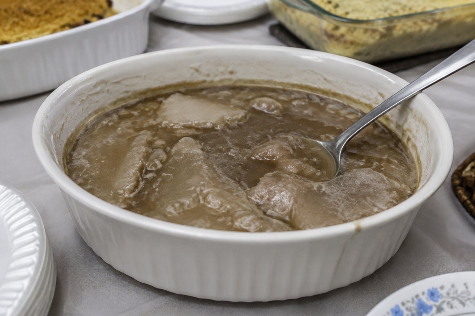 A bowl of thick, congealed brown gravy sits on a potluck buffet table.