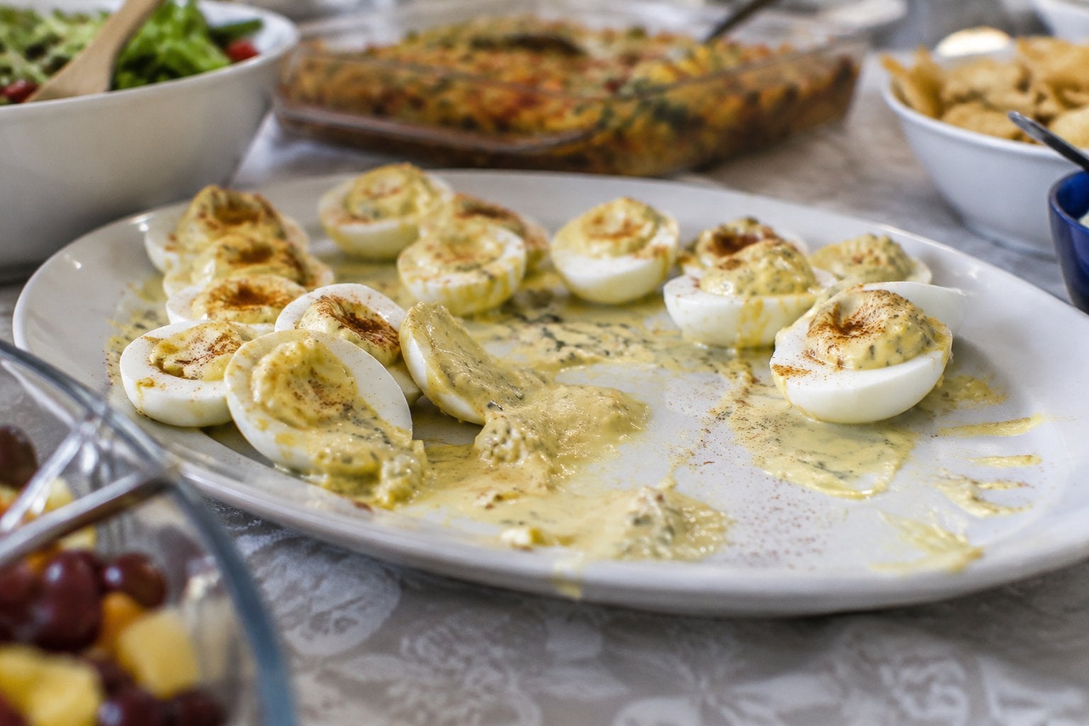 A platter of deviled eggs with filling that has run onto the plate.
