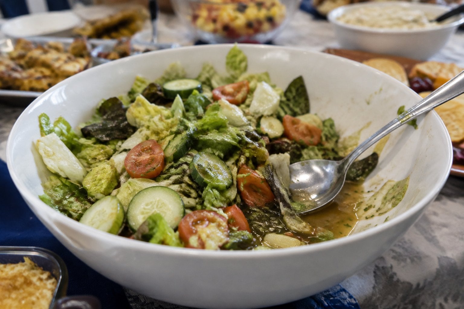 A bowl of wilted garden salad sits on a potluck buffet table.