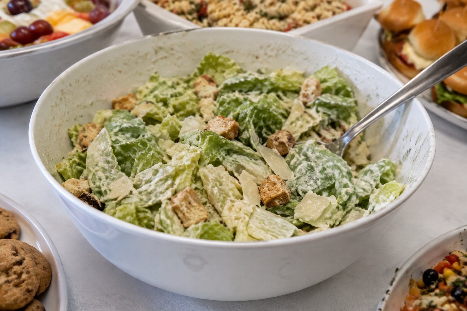 A bowl of wilted Caesar salad with soft croutons sits on a buffet table.