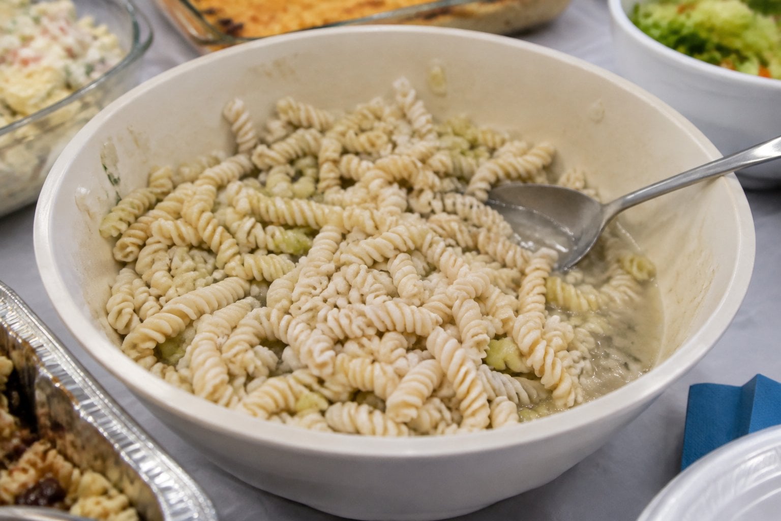 A bowl of plain pasta salad on a potluck table.