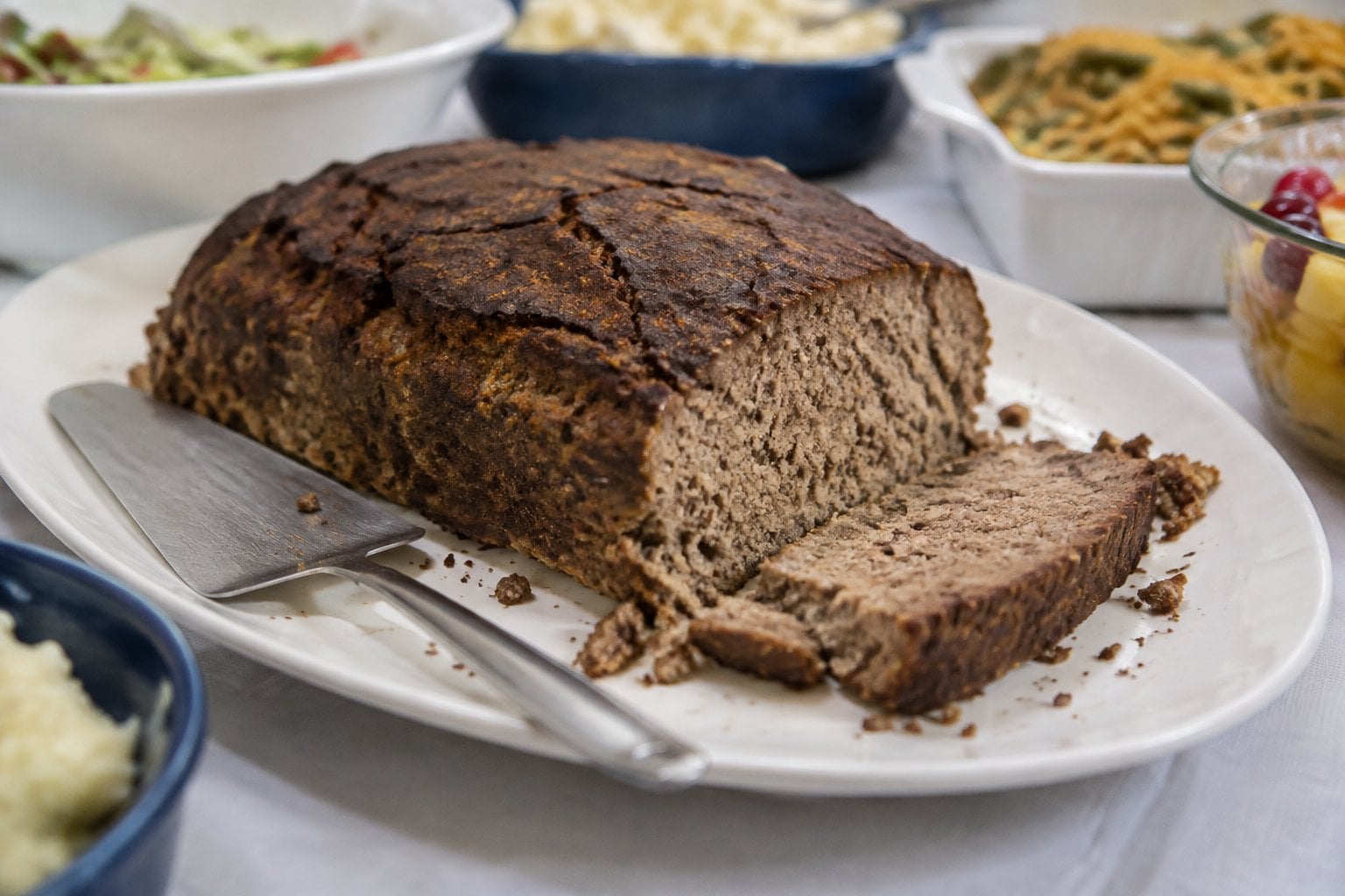 A dry, crumbly meatloaf sits on a serving platter at a potluck buffet.