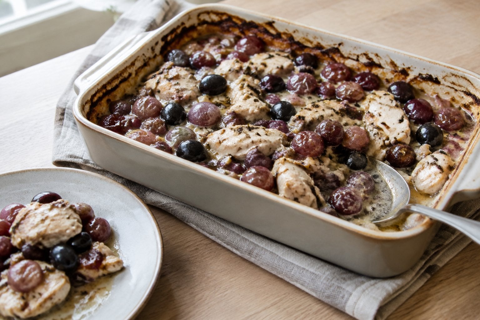 A casserole of chicken, dark olives, and purple grapes.