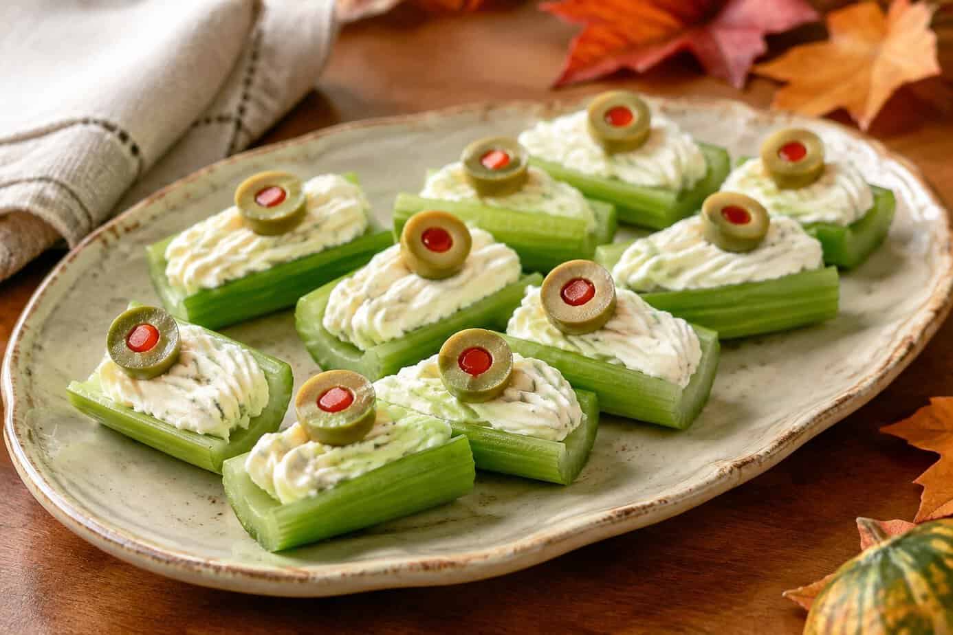 Celery sticks filled with cream cheese and topped with green olives on a platter.