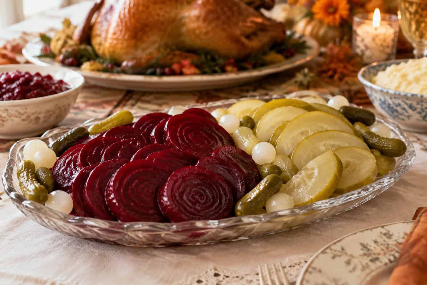 A glass platter of pickled beets and watermelon rind pickles on a Thanksgiving table.