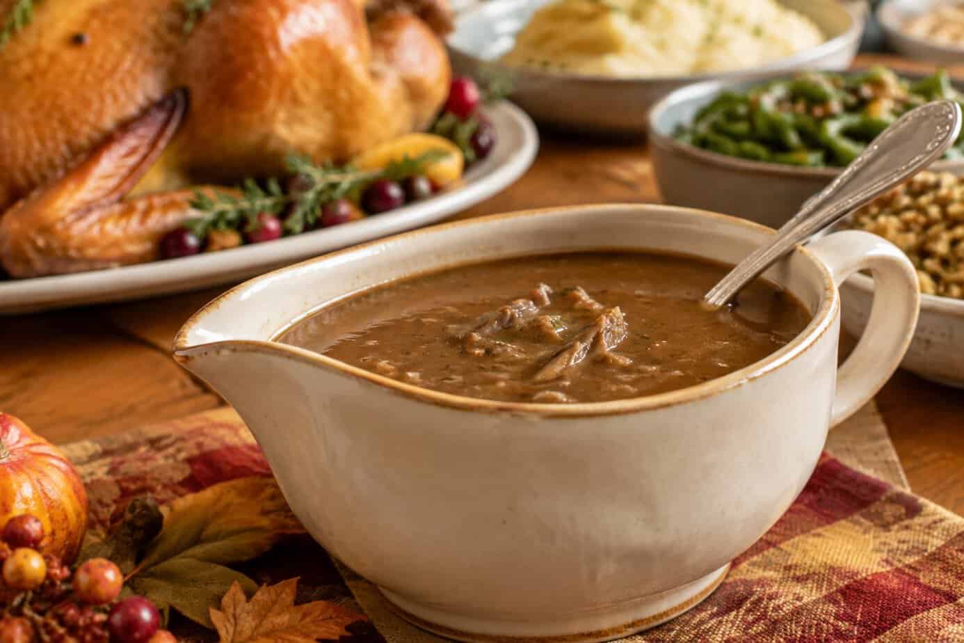 A ceramic gravy boat filled with giblet gravy sits on a Thanksgiving table.